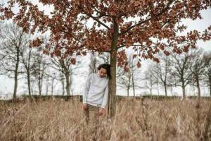 A man leans sadly against a tree