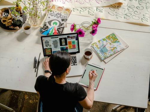 Female sat at desk working on computer writing on notepad